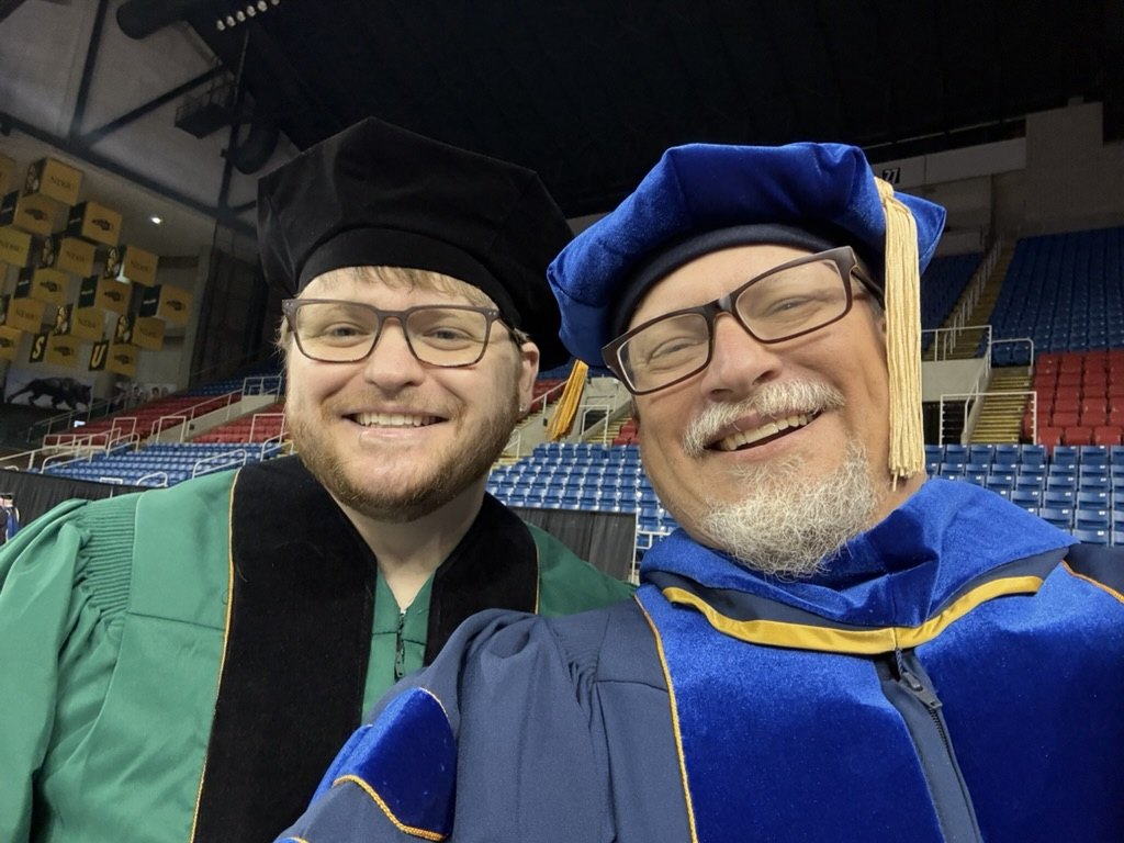 Garrett Byron and Clayton Hilmert in academic regalia at NDSU commencement