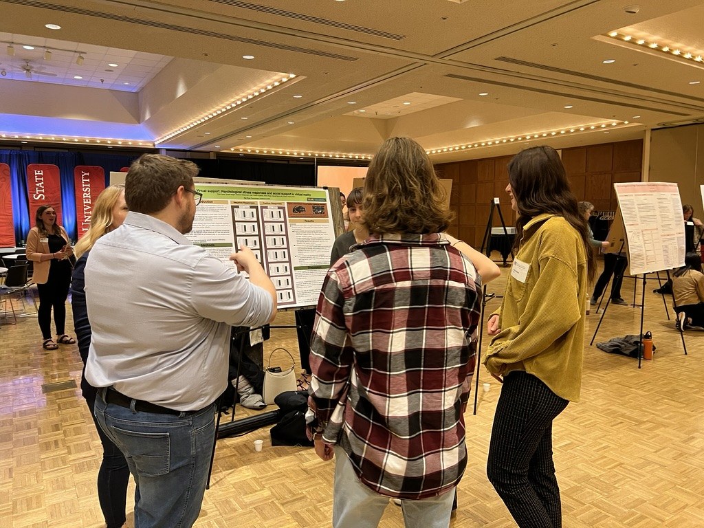 Lab members discussing the virtual support poster with visitors at the 2024 Red River Psychology Conference